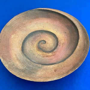 Op de afbeelding: Een bruin keramiek bord met een spiraalvormig ontwerp in tinten bruin, geel en roze.