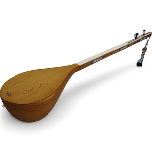 May include: A wooden stringed instrument with a pear-shaped body and a long neck. The instrument has a light brown finish with decorative elements on the neck and a tassel at the end. The text "Kabul Gallery" is visible on the body.