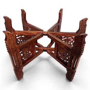 May include: A brown wooden folding stand featuring four legs with intricate carved floral patterns. The structure consists of two interlocking pieces that form a cross-shaped base, designed to support a bowl or object in an elevated position.