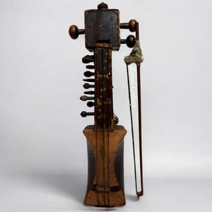 May include: A brown wooden sarangi, a stringed musical instrument from India, with a carved wooden body and a long neck with multiple strings. The instrument is shown with a bow.