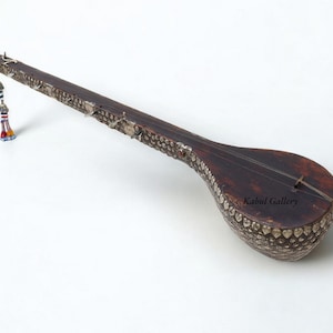 Op de afbeelding: Een langnekkige, houten snaarinstrument met een rond lichaam. Het lichaam is versierd met zilverkleurige metalen accenten. Het instrument heeft een kwast gemaakt van gekleurde kralen.