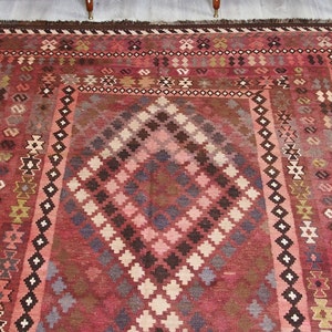 May include: A traditional red, brown, and cream colored rug with a geometric pattern. The rug has a fringe border.