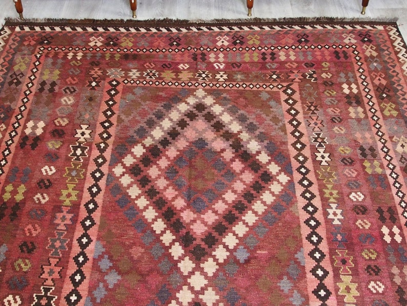 May include: A traditional red, brown, and cream colored rug with a geometric pattern. The rug has a fringe border.
