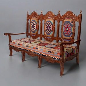 May include: A wooden couch with a carved back and armrests. The couch is upholstered in a colorful patterned fabric with geometric designs.
