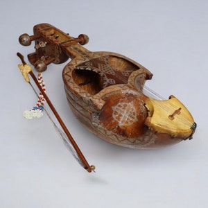 May include: A brown wooden stringed instrument with intricate carvings and a beaded bow. The instrument is called a sarangi and is a popular instrument in Indian classical music.