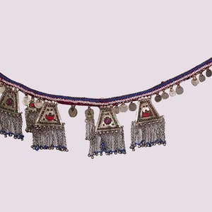 Può includere: Una cintura di perline argentate e blu con un bordo rosso e bianco. La cintura ha una serie di monete d'argento e ciondoli triangolari con accenti rossi e blu.