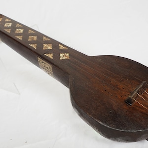 May include: A long, wooden musical instrument with a rounded body and a long neck. The neck is decorated with intricate metalwork. The instrument has a single string and a bridge.