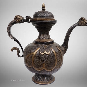 May include: An ornate, black and gold metal teapot with a dragon-shaped spout and handle. The teapot is decorated with intricate floral and geometric patterns, and the inscription "Allah" is visible on the body.