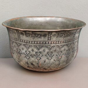 Könnte beinhalten: Eine silberne Schale mit aufwendigen schwarzen und roten Designs. Die Schale hat eine abgerundete Form und einen leicht ausgestellten Rand.
