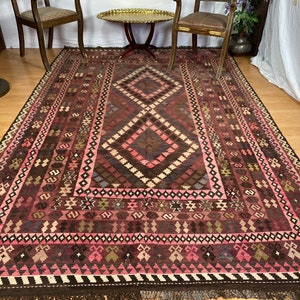 May include: A traditional Turkish rug with a geometric pattern in shades of pink, brown, and white. The rug has a fringe border and is woven with intricate details.