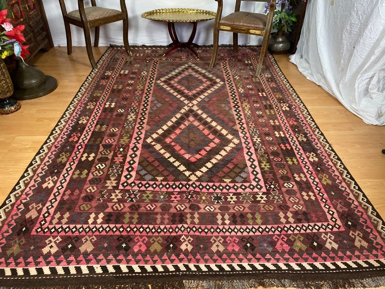 May include: A traditional Turkish rug with a geometric pattern in shades of pink, brown, and white. The rug has a fringe border and is woven with intricate details.