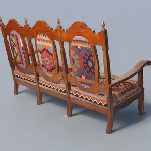 May include: A three-seater wooden sofa with a carved back and armrests. The sofa is upholstered in a colorful patterned fabric with geometric designs in shades of red, blue, green, and yellow.