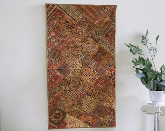 May include: A tapestry wall hanging with a patchwork design of various shades of brown, red, and blue. The tapestry is made of fabric scraps sewn together in a geometric pattern.