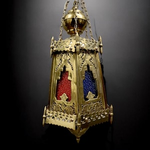 Może przedstawiać: Złota metalowa lampa wisząca z misternymi wzorami i czerwonymi i niebieskimi szklanymi panelami.