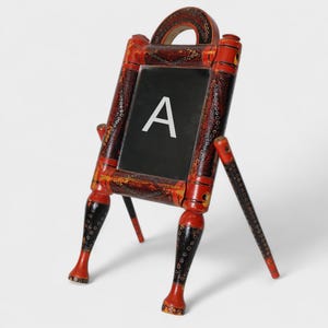May include: A red and black wooden easel with a chalkboard panel. The chalkboard has the letter "A" written on it.