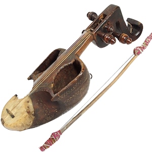 Op de afbeelding: Een bruin houten snaarinstrument met een gesneden houten body en een enkele snaar. Het instrument heeft een decoratief ontwerp op de body en wordt vastgehouden door een houten strijkstok.