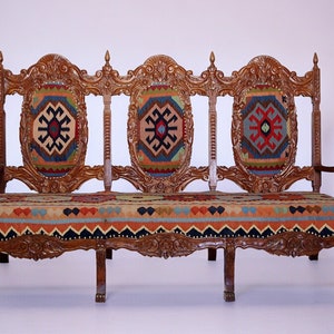 May include: A wooden three-seater sofa with intricate carvings and a colorful patterned fabric upholstery.
