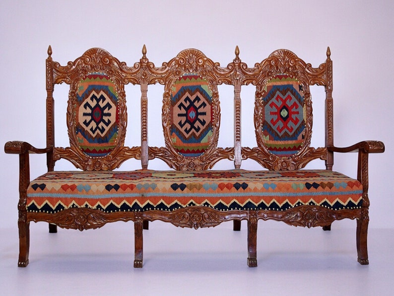 May include: A wooden three-seater sofa with intricate carvings and a colorful patterned fabric upholstery.