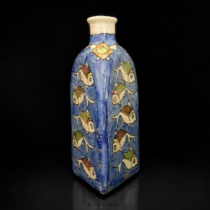 May include: A blue ceramic vase with a white rim and a geometric design of colorful fish. The vase is decorated with a repeating pattern of fish swimming in a blue background.