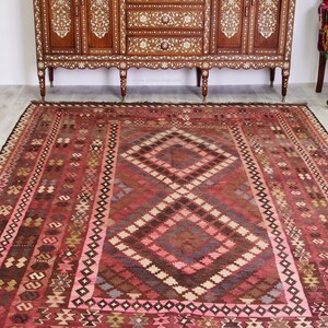 May include: A traditional red, pink, and brown patterned rug with a diamond-shaped design in the center. The rug has a fringe border.
