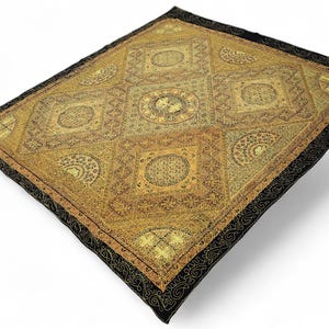 May include: A square textile with a detailed, geometric pattern in gold and black. The central design features repeating squares and circles with intricate floral and abstract motifs. The border is black with a scrolling design.