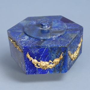 Op de afbeelding: Een zeshoekige doos gemaakt van lapis lazuli met gouden accenten. De doos heeft een scharnierend deksel en is versierd met ingewikkelde bloemmotieven.
