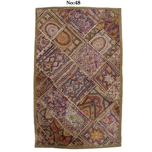 May include: A colourful patchwork wall hanging with a gold border. The fabric is made of different textures and patterns, including embroidered flowers, stars, and geometric shapes. The wall hanging is decorated with small mirrors.