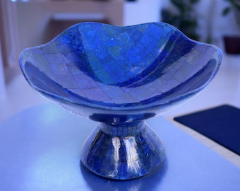 May include: A blue mosaic bowl with a pedestal base. The bowl has a unique, wavy rim and is made of small, square tiles in varying shades of blue. The base is a matching blue, creating a cohesive and elegant design. The text "Kabul Gallery" is visible.