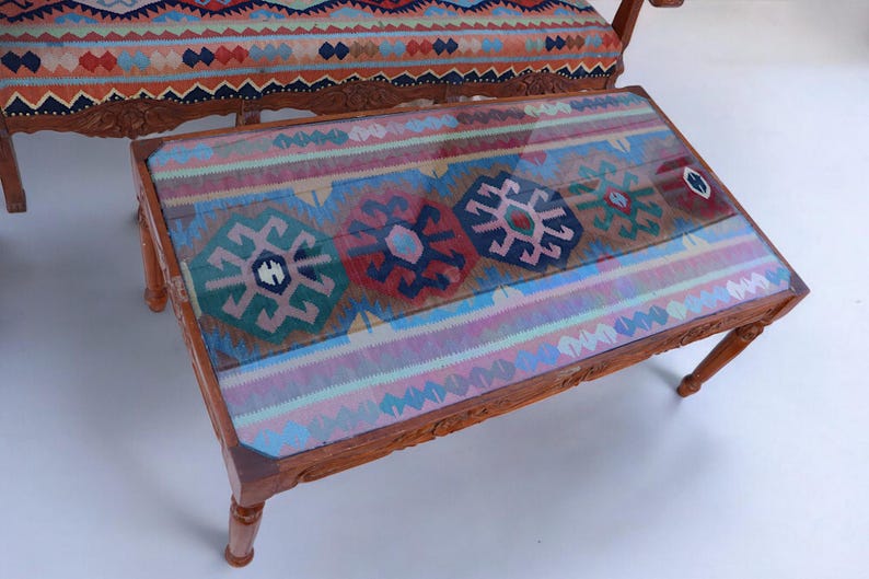 May include: A wooden coffee table with a glass top and a colorful patterned rug inset. The rug has a geometric design with shades of blue, red, green, and pink.
