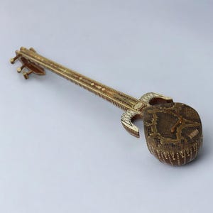 Op de afbeelding: Een houten muziekinstrument met ingewikkelde houtsnijwerk en een bruin, gepatroneerd lichaam. Het instrument heeft een lange nek en een rond lichaam.