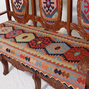 May include: A wooden bench with a carved frame and a colorful patterned cushion. The cushion is made of a woven fabric with geometric designs in shades of red, blue, green, and yellow.