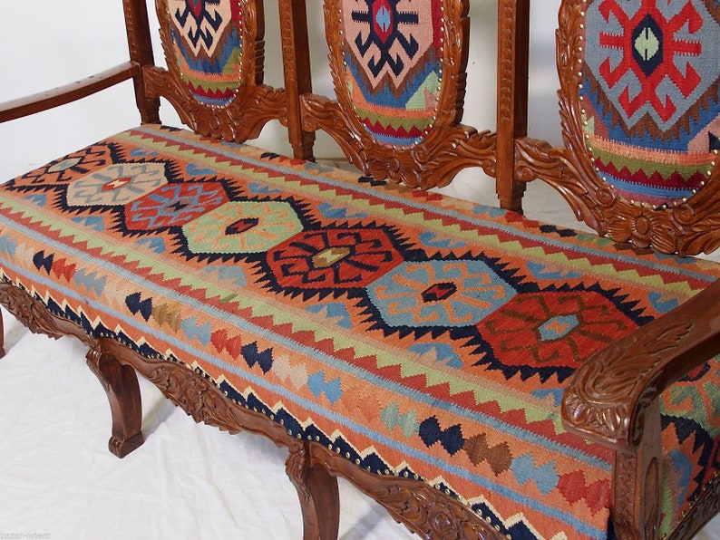 May include: A wooden bench with a carved frame and a colorful patterned cushion. The cushion is made of a woven fabric with geometric designs in shades of red, blue, green, and yellow.