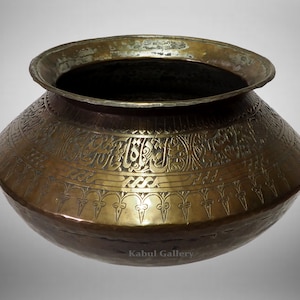 May include: A large, round, brass pot with intricate engraved designs. The pot has a wide, flat base and a narrow opening. The designs include Arabic calligraphy and floral motifs.