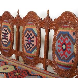 May include: A wooden bench with three carved backrests and a patterned cushion. The backrests are decorated with intricate carvings and the cushion is made of a colorful fabric with a geometric design.