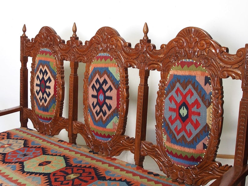 May include: A wooden bench with three carved backrests and a patterned cushion. The backrests are decorated with intricate carvings and the cushion is made of a colorful fabric with a geometric design.
