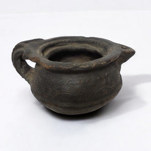 Può includere: Un piccolo vaso in ceramica marrone scuro con un manico e un beccuccio. Il vaso ha un motivo decorativo all'esterno.