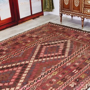 May include: A traditional red, brown, and cream colored rug with a geometric pattern. The rug has a diamond shape in the center and is surrounded by a border of smaller diamonds.