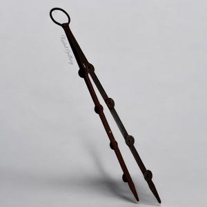 Op de afbeelding: Een tang van roestig metaal met een ringvormige handgreep. De tang is gesloten en heeft een puntige punt.