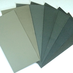 Peut inclure: Assortiment de feuilles de papier de verre dans différentes nuances de vert et de gris. Les feuilles sont disposées en éventail, la nuance la plus claire en haut et la nuance la plus foncée en bas.