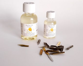 May include: Two bottles of Zest-It Dip Pen Nib Cleaner, one 125 ml and one 50 ml, with a pile of dip pen nibs on a white surface. The bottles are clear and have white labels with black text. The text on the labels reads "Dip Pen Nib Cleaner" and "Zest-It". The nibs are made of metal and are various sizes and shapes.