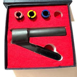 Könnte beinhalten: Ein schwarzes Werkzeugset mit roten, gelben und blauen Komponenten, präsentiert in einer schwarzen Box mit rotem Samtinterieur. Das Set enthält ein hebelartiges Werkzeug und mehrere kleine, kreisförmige Teile.