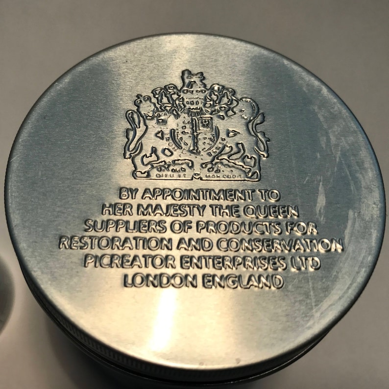 K&ouml;nnte beinhalten: Ein silberner Metallbeh&auml;lterdeckel mit dem k&ouml;niglichen Wappen und dem Text "By Appointment to Her Majesty The Queen Suppliers of Products for Restoration and Conservation Picreator Enterprises Ltd London England".