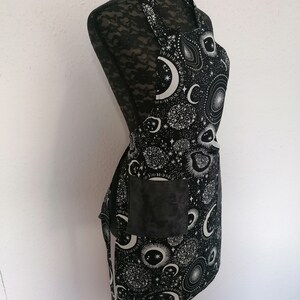 May include: Black apron with a white moon and stars print. The apron has a large pocket on the front.