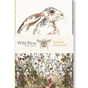 May include: A Wild Press stitched notebook with a floral hare illustration. The notebook is wrapped with a band displaying the brand name, a bee illustration, and the words "Stitched Notebook". The bottom of the notebook features a colorful design of various flowers and foliage.