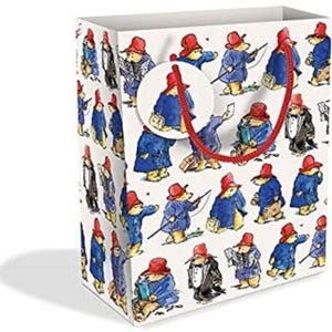 May include: A white gift bag with a red handle and a repeating pattern of Paddington Bear wearing a blue coat and red hat. The bag is decorated with a small circle with a Paddington Bear image.