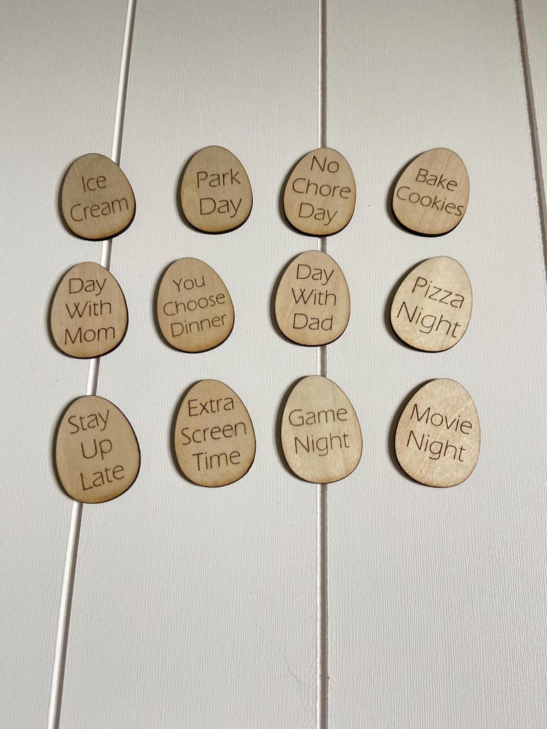 Op de afbeelding: Houten fiches met verschillende activiteiten erop geschreven, zoals "IJs", "Dagje uit", "Geen klusjesdag", "Koekjes bakken", "Dag met mama", "Jij kiest het diner", "Dag met papa", "Pizza avond", "Laat opblijven", "Extra schermtijd", "Spelletjesavond" en "Filmavond".