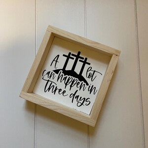 Puede incluir: Un letrero de madera blanco con un dise&ntilde;o pintado en negro de tres cruces y el texto "Mucho puede pasar en tres d&iacute;as".