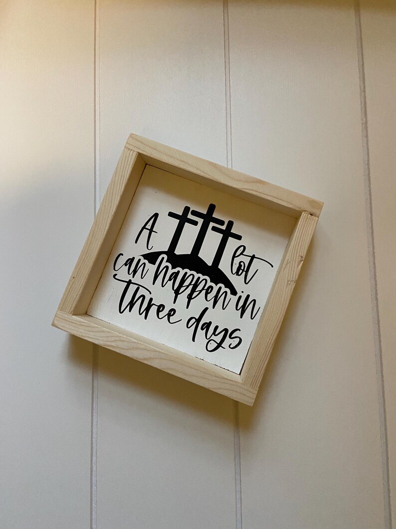 Puede incluir: Un letrero de madera blanco con un dise&ntilde;o pintado en negro de tres cruces y el texto "Mucho puede pasar en tres d&iacute;as".