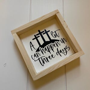 Puede incluir: Un letrero de madera con fondo blanco y letras negras. El letrero dice "A lot can happen in three days" con tres cruces sobre el texto.