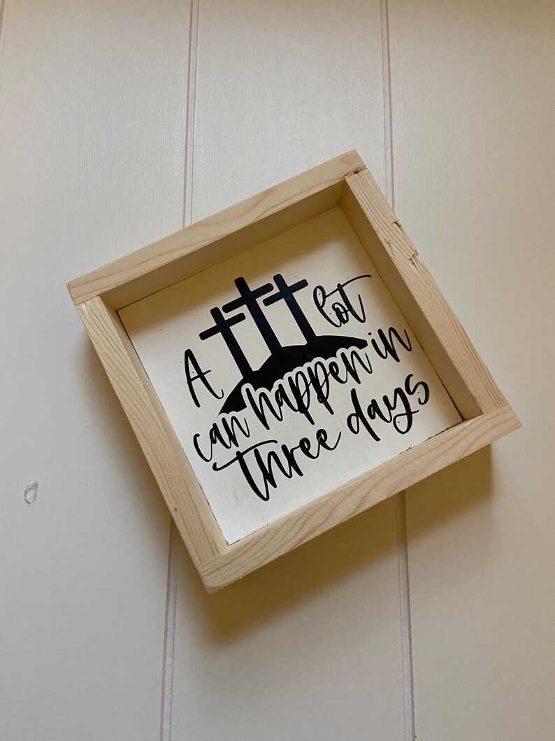 Puede incluir: Un letrero de madera con fondo blanco y letras negras. El letrero dice "A lot can happen in three days" con tres cruces sobre el texto.